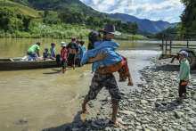 A refugee carries his grandmother to the shore of Mizoram, India, after crossing Tiau River from Myanmar
