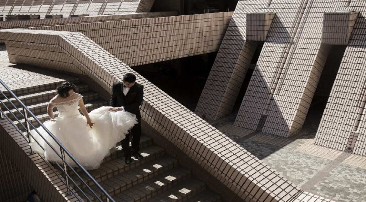 A groom helps his bride with her wedding dress as they walk down stairs during a photo shoot at the Hong Kong