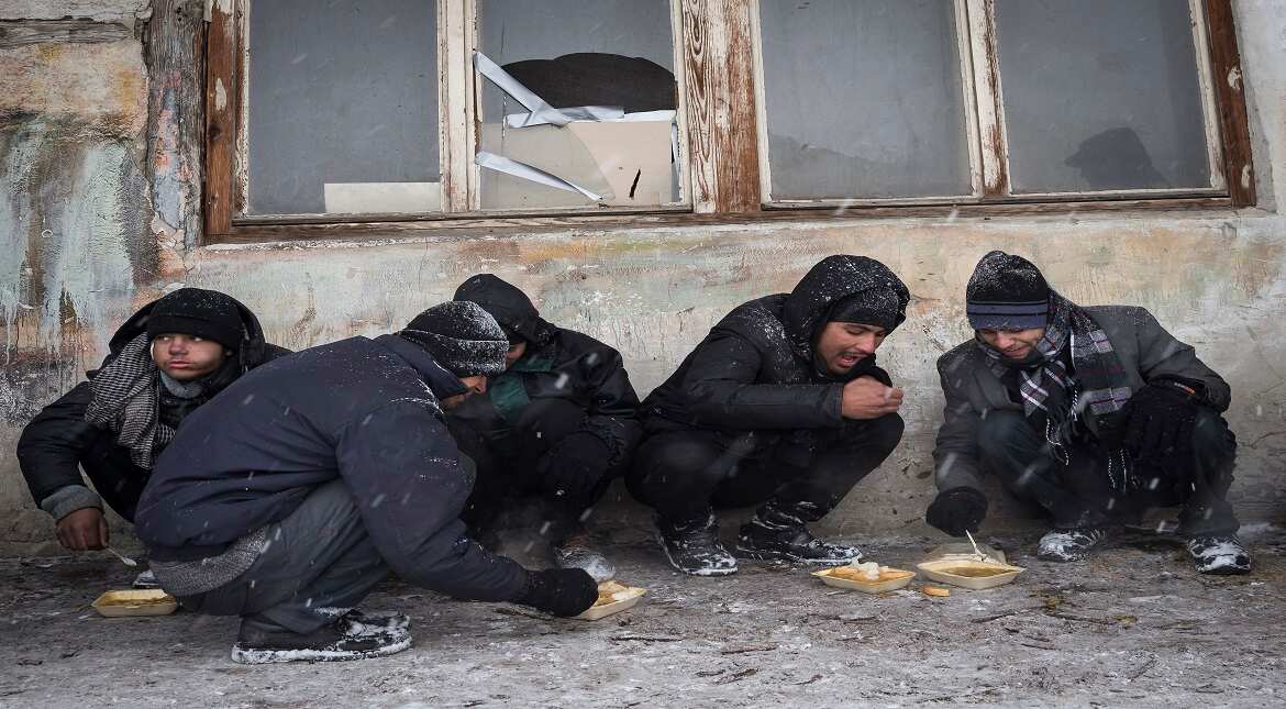 Migrants eats  plates of free food as snow falls outside a derelict customs warehouse in Belgrade, Serbia.