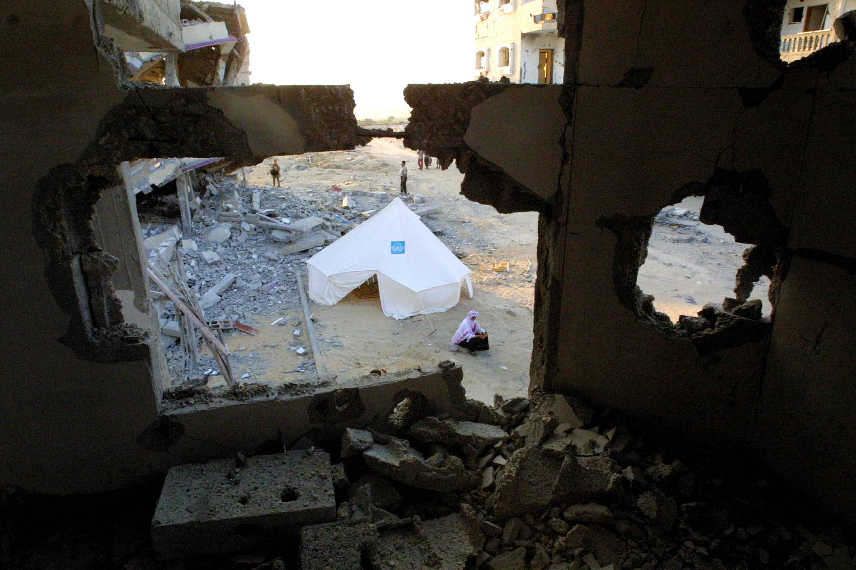 A Palestinian woman living in a tent is seen through damage inflicted on her home by an Israeli tank August 27, 2002 in the Khan Younis refugee camp in the southern Gaza Strip.