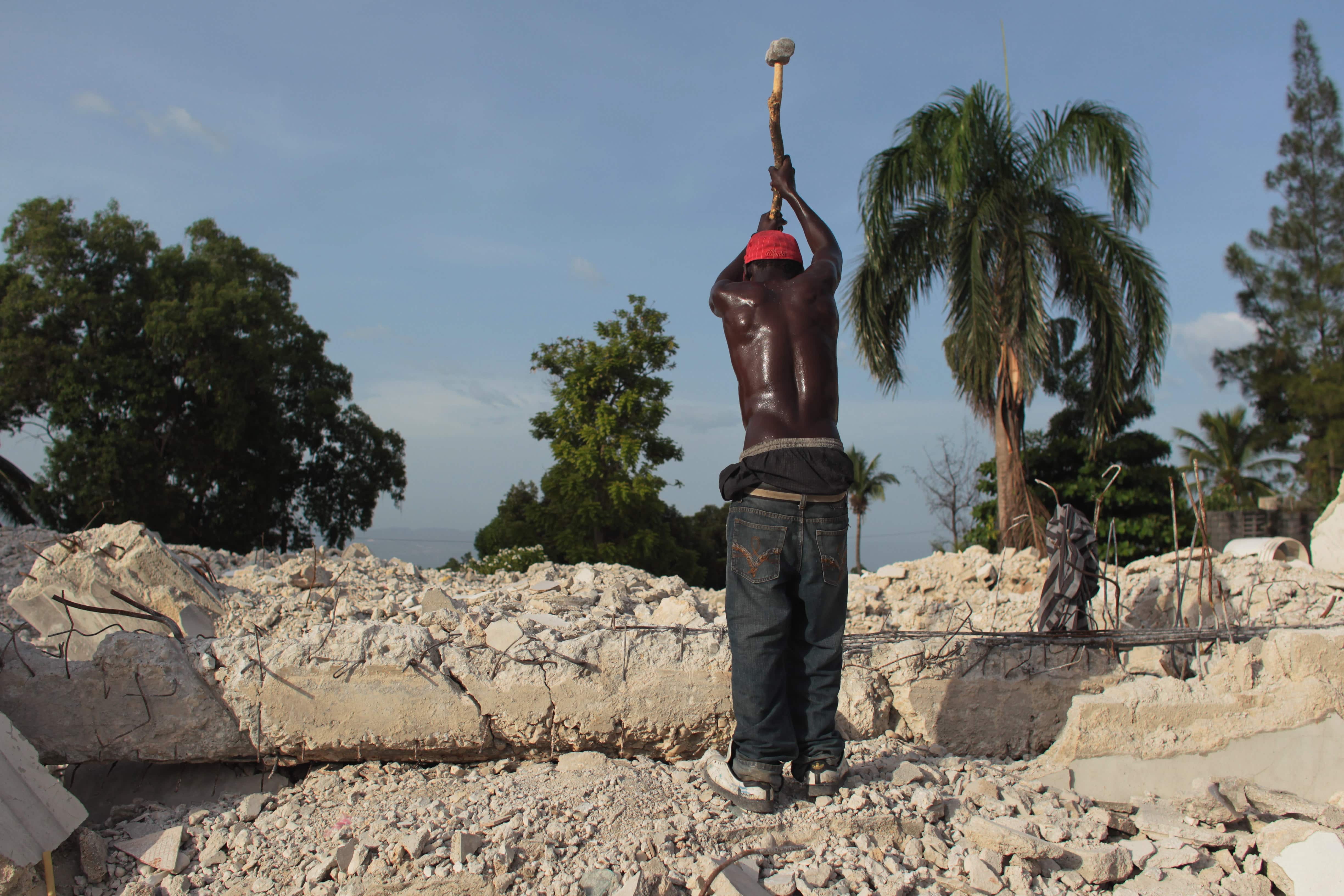 A man uses a sledge hammer to break a building that collapsed during the 2012 earthquake in Port-au-Prince, Haiti. Over 1.5 million survivors had to live in tent camps.