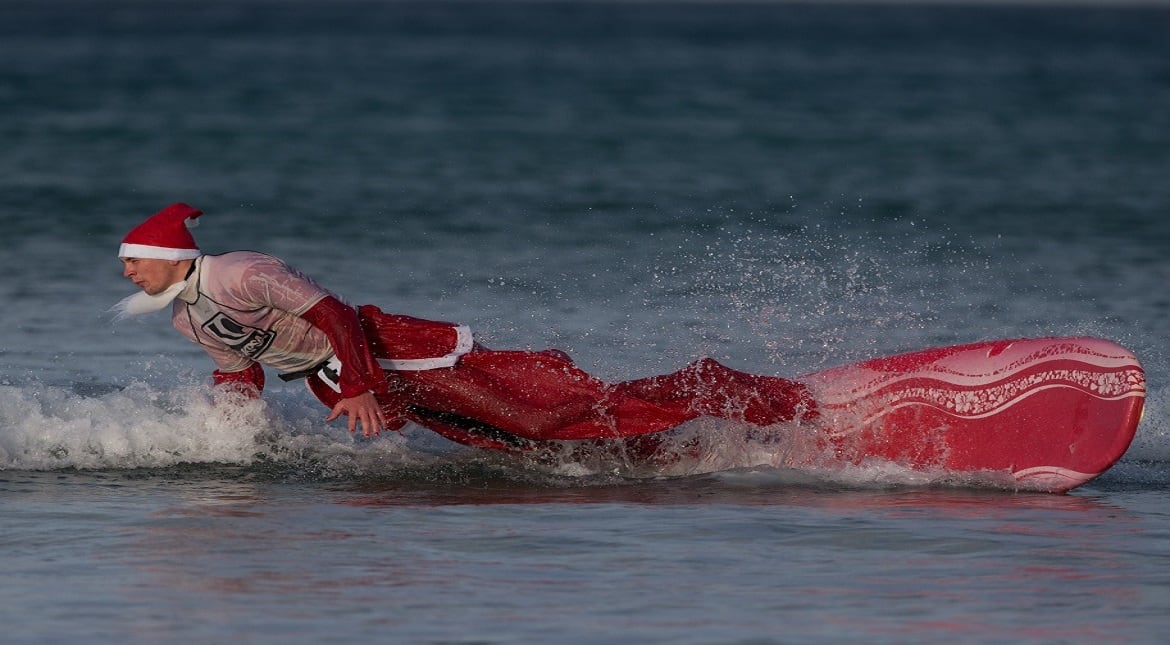 A surfer dressed as Santa falls off his surfboard as he braves the