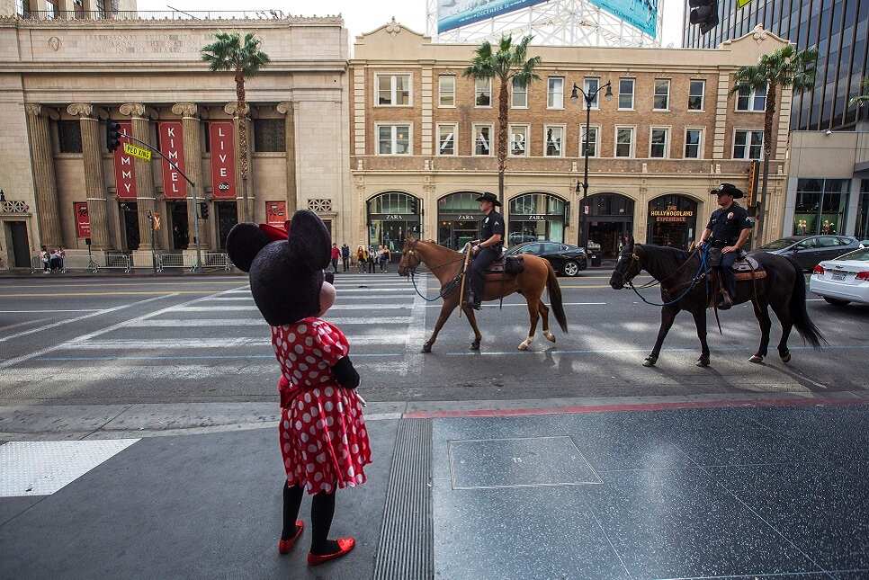 Los Angeles Police Department Mounted Platoon officers ride past a Minnie Mouse character near the