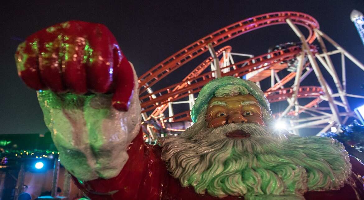 A life size figure of Father Christmas in front of a roller coaster at the Winter Wonderland in Hyde Park in London, England.