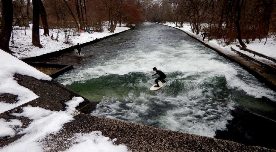 Surfers ride the Eisbach canal wave during freezing conditions on the Isar River in the English Garden in Munich