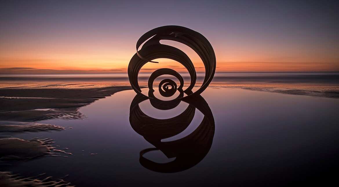 The sun sets behind the semi-submerged Mary's Shell sculpture on Cleveleys Beach in Blackpool, England.