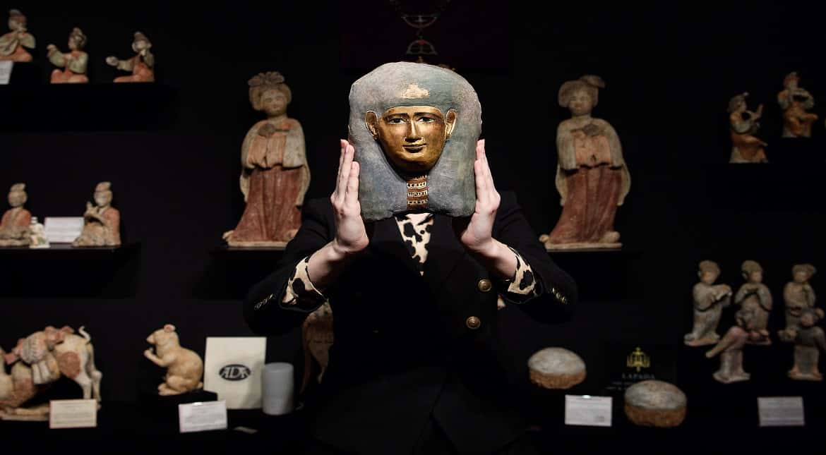 An Egyptian child's mummy mask from 305-30BC is held up at the Mayfair Antiques and Fine Art Fair in London, England.