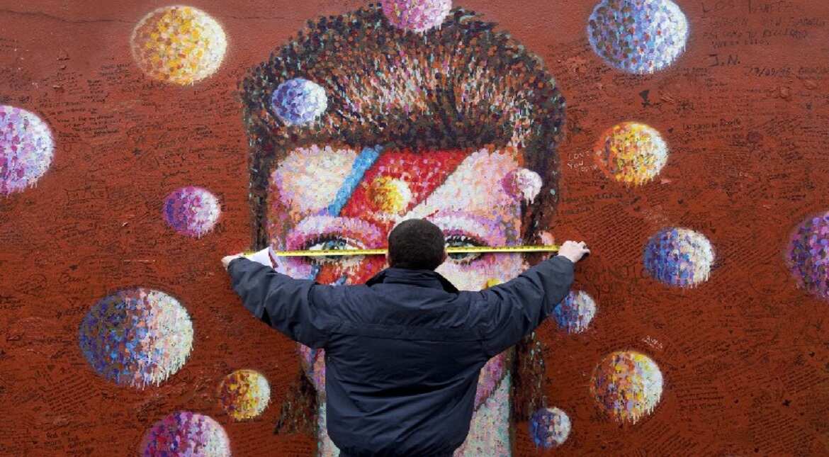 A workman measures up a mural of British musician David Bowie by Australian