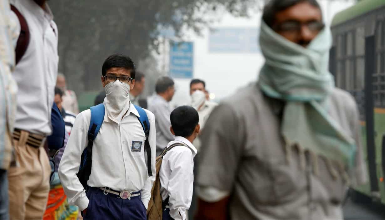 A schoolboy covers his face with a handkerchief as he waits for a passenger bus