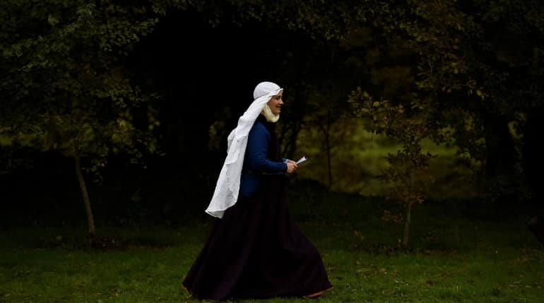 A woman dressed in medieval costume walks with a book