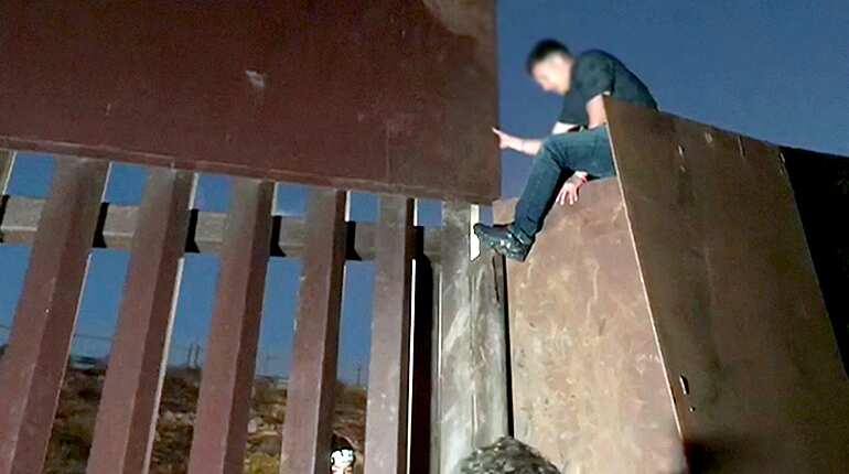 Dramatic video shows migrants jumping the border fence at night as Border Patrol looks on