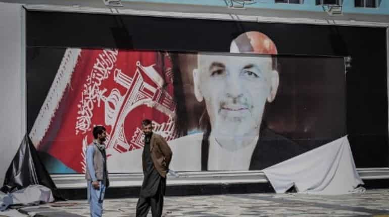 Men stand next to the a torn poster of Ashraf Ghani