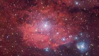 A rosy red nebula dotted with bright twinkling stars presents a captivating image