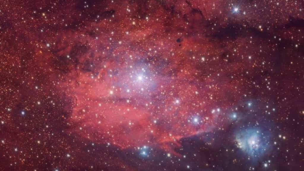 A rosy red nebula dotted with bright twinkling stars presents a captivating image