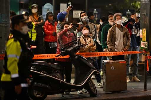  Onlookers stand behind a police cordon as they use their mobile phones to take photos of the site of a Halloween stampede. 