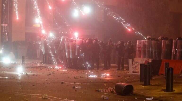 Fireworks are set off in front of police officers standing in position behind riot shields during the protest