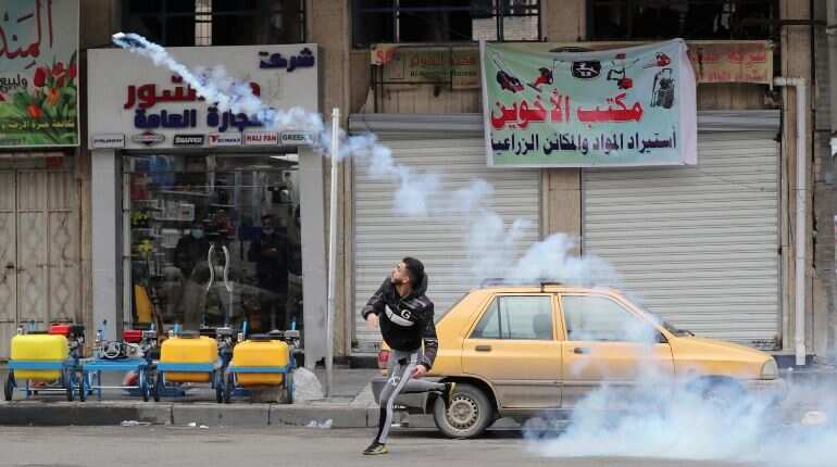 Demonstrator throws a tear gas canister back at the Iraqi security forces